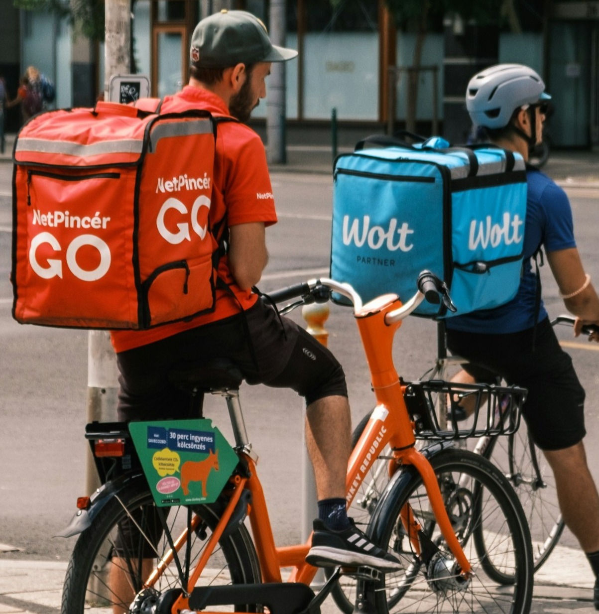 A delivery rider on a scooter carrying a delivery bag with the Chompyum Food Express logo, navigating through a bustling city street. The rider should have a friendly smile and be wearing a helmet. The background should be a dynamic city scene with other vehicles and people, emphasizing the speed and convenience of the delivery service.